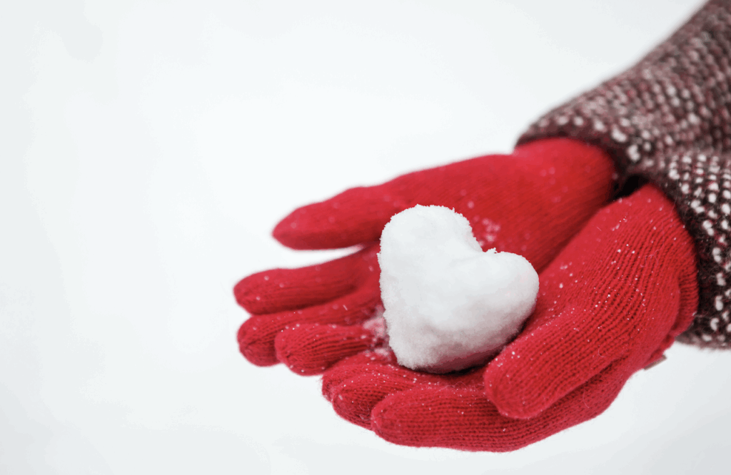 Photo of red gloved hands holding a snowball in the shape of heart