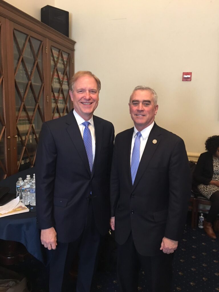 Photo of two men standing next to each other and smiling while wearing black suits