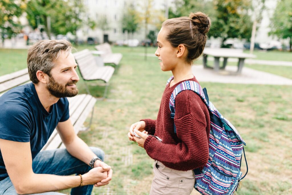 Photo of a man sitting on a bench while talking to a young girl
