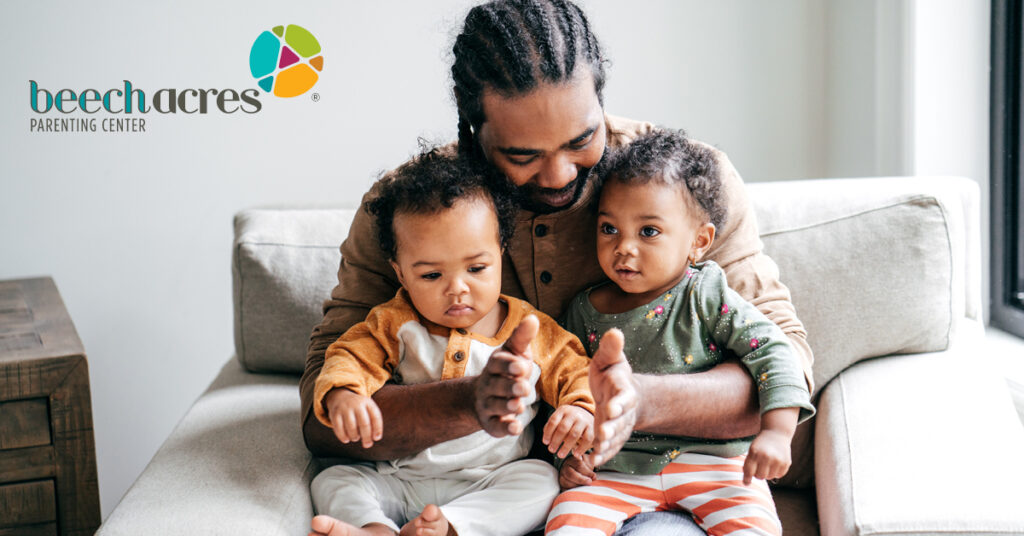 Photo of a man holding two babies with the BAPC logo in the corner