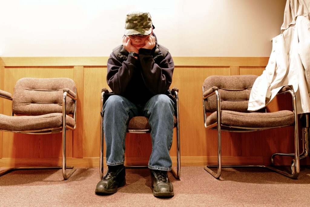 Photo of an unhappy teen boy sitting in a chair with his hands on his face