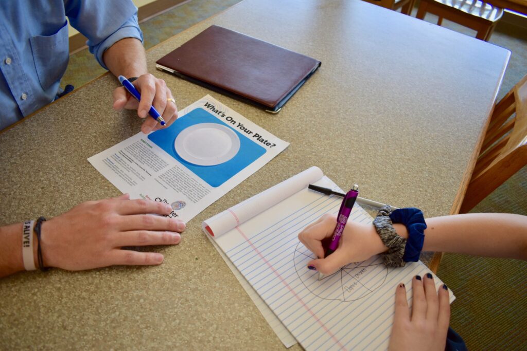 Photo of a child's hands drawing a pie chart with a grown-up's hands holding an activity sheet