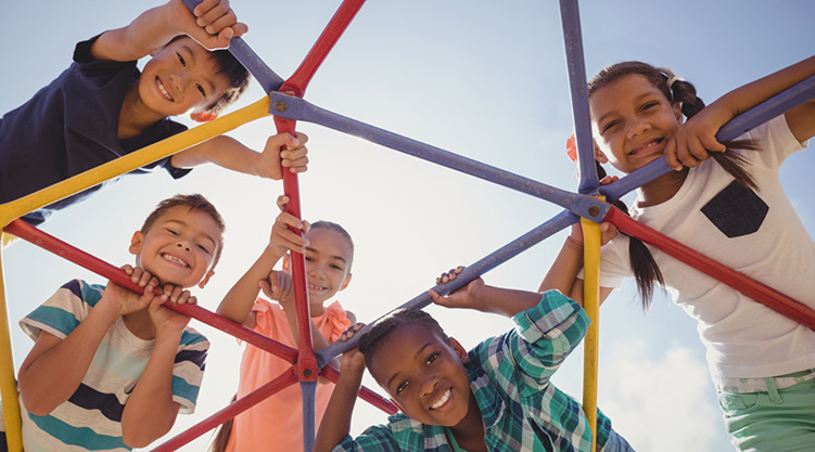 Photo of young children smiling while standing and hanging on playground equipment