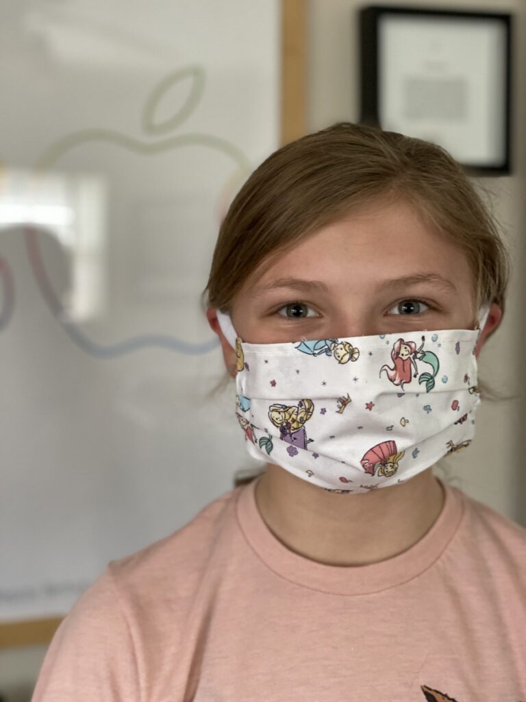 Photo of. young girl wearing a face mask with mermaids on it