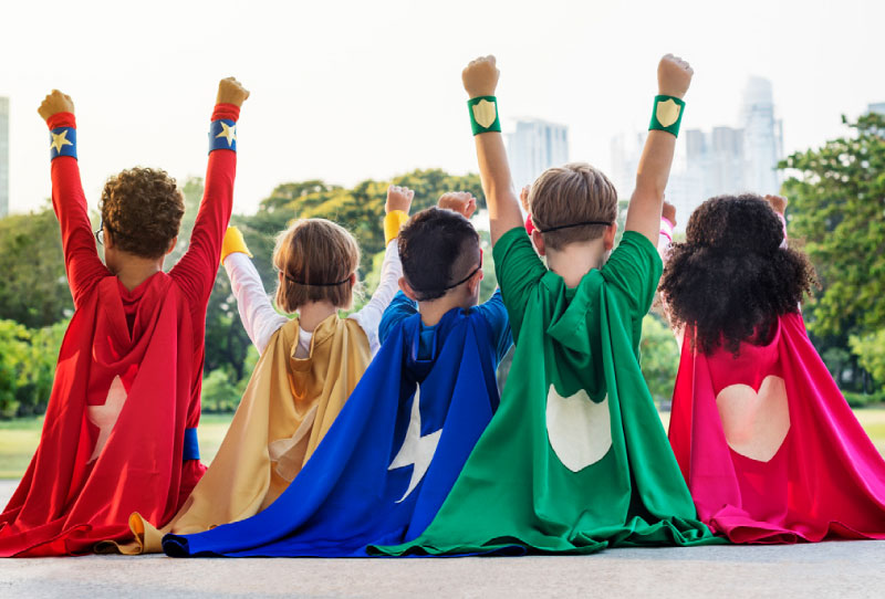 Photo of five children dressed like superheroes with their arms in the sky