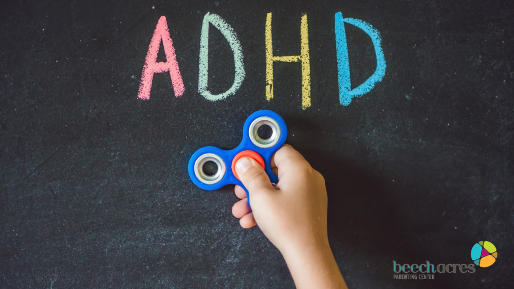 Photo of a child's had holding a fidget spinner with the word ADHD written on a chalkboard in the background