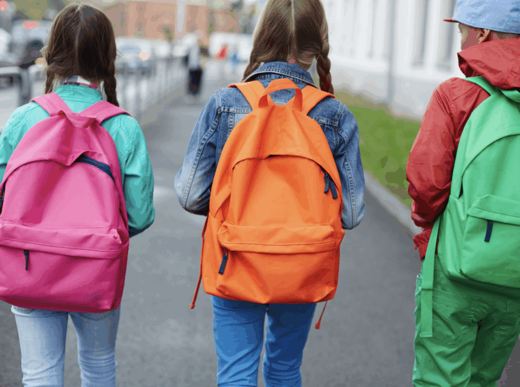 Photo of three children with backpacks on walking outside of their school