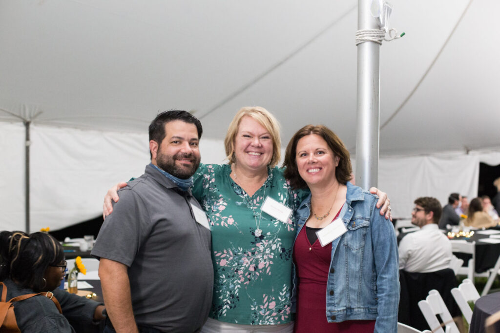 Photo of two women and a man smiling with their arms around each other