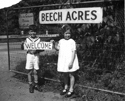Black and white photo of a young girl and boy holding up a welcome sign in front of Beech Acres