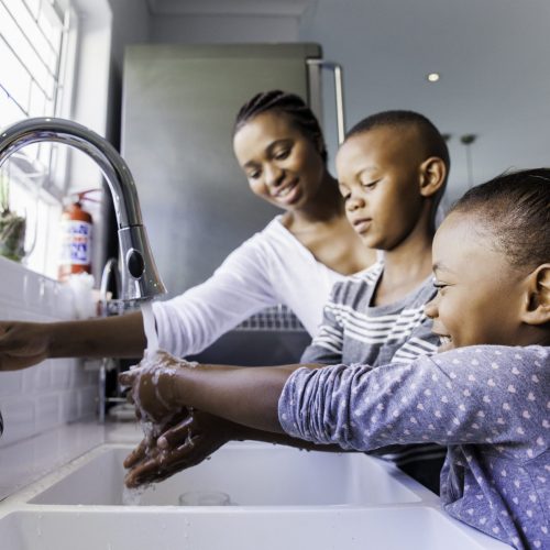 Photo of a mother turning on a sink faucet as her two children hold out their hands to wash them
