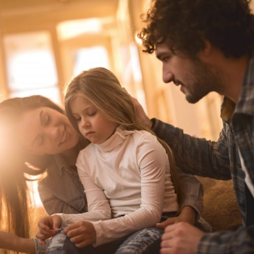 Photo of two parents telling their child about their divorce as the child frowns